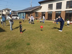 中学生が芝生で子どもとボール遊びをするようす